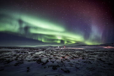 Erstaunlicher Anblick des Polarlichts, das am Nachthimmel mit Sternen über einem schneebedeckten Berg im Winter in Island leuchtet - ADSF37404