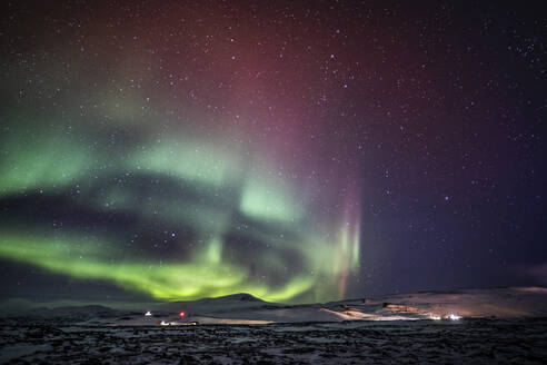 Erstaunlicher Anblick des Polarlichts, das am Nachthimmel mit Sternen über einem schneebedeckten Berg im Winter in Island leuchtet - ADSF37405