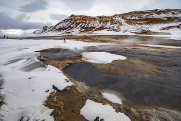 Unkenntlich gemachter Reisender, der in einem Gelände mit geothermischen Quellen steht, aus denen Dampf austritt, und in die Kamera schaut, während er in Island unterwegs ist - ADSF37407