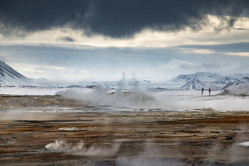 Unkenntlich gemachter Reisender, der in einem Gelände mit geothermischen Quellen steht, aus denen Dampf austritt, und in die Kamera schaut, während er in Island unterwegs ist - ADSF37408
