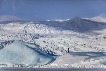 Unrecognizable traveler hiker admiring spectacular scenery of frozen seashore with ice and snow in winter in Iceland - ADSF37414