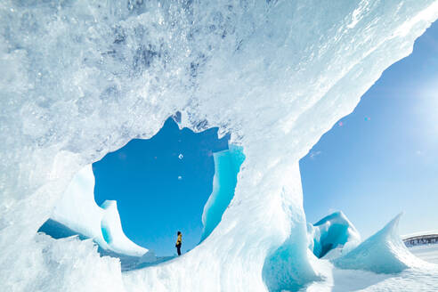 Unbekannter Wanderer bewundert die spektakuläre Landschaft der gefrorenen Meeresküste mit Eis und Schnee im Winter in Island - ADSF37418