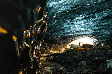 Fernblick auf einen unerkennbaren Reisenden, der im Winter in einer Eishöhle steht, während eines Urlaubs in Island - ADSF37420