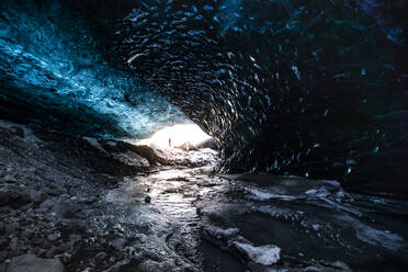 Fernblick auf einen unerkennbaren Reisenden, der im Winter in einer Eishöhle steht, während eines Urlaubs in Island - ADSF37421