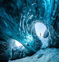 Fernblick auf einen unerkennbaren Reisenden, der im Winter in einer Eishöhle steht, während eines Urlaubs in Island - ADSF37423