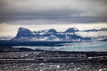 Arctic landscape of blocks of ice floating on lake surrounded by rough rocky cliffs under cloudy sky in Iceland - ADSF37425