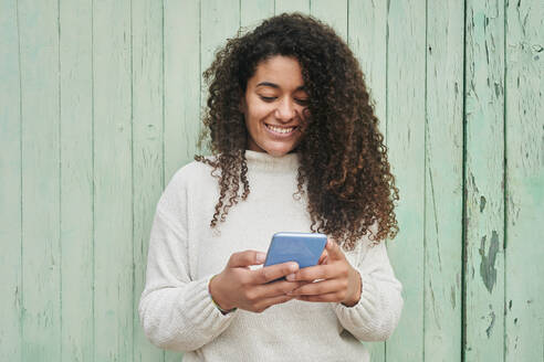 Lächelnde Frau, die ein Smartphone benutzt und vor einer Holzwand steht - KIJF04500