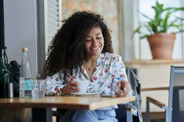 Glückliche junge Frau mit Kaffeetasse im Café sitzend - KIJF04501
