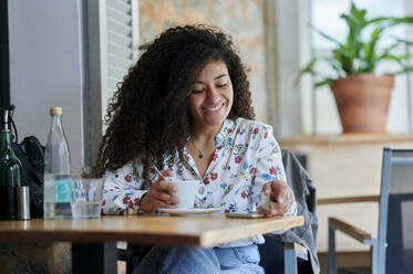 Happy young woman sitting with coffee cup at cafe - KIJF04501