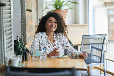 Glückliche junge Frau mit Kaffeetasse in einem Café sitzend - KIJF04503