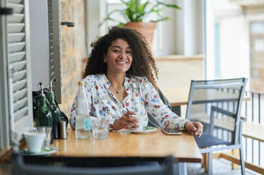 Happy young woman with coffee cup sitting at cafe - KIJF04503