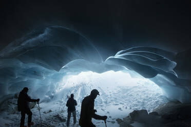 Silhouetted men hiking in glacier ice cave, Selkirk Mountains, Canada - FSIF06111