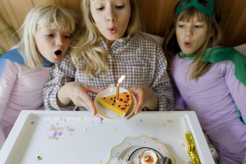Mutter mit Kindern beim Ausblasen einer Kerze auf einem Kuchen zu Hause - TYF00412