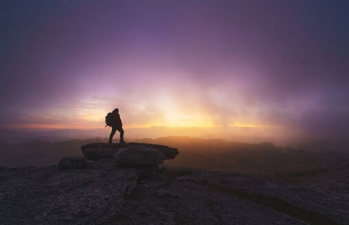 Seitenansicht einer Silhouette eines männlichen Spähers auf einem Bergfelsen bei Sonnenaufgang - ADSF37484