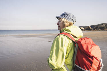 Ältere Frau mit Rucksack am Strand stehend - UUF27184