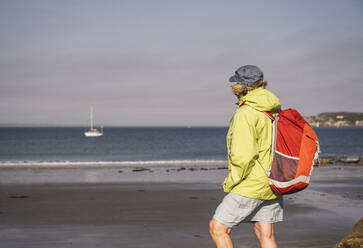 Ältere Frau mit Rucksack am Strand stehend an einem sonnigen Tag - UUF27188