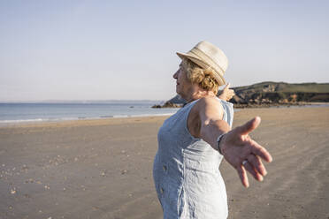 Senior woman with arms outstretched standing at beach - UUF27208