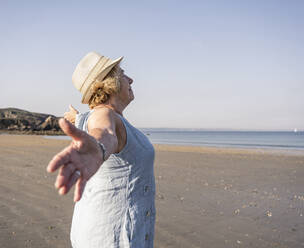 Senior woman with arms outstretched standing at beach on sunny day - UUF27209