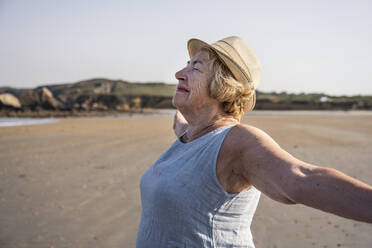 Smiling woman with arms outstretched enjoying at beach - UUF27210