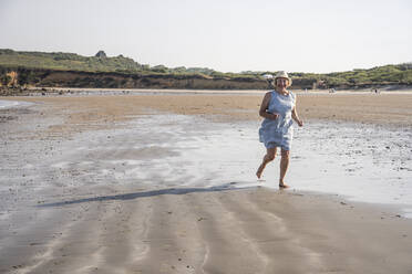 Active senior woman running at beach on sunny day - UUF27216