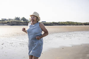 Aktive ältere Frau springt am Strand - UUF27218