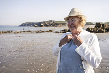 Happy senior woman wearing hat on vacation at beach - UUF27221
