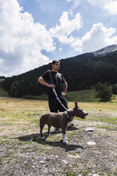 Mann steht mit Hund vor einem Berg an einem sonnigen Tag - PNAF04500