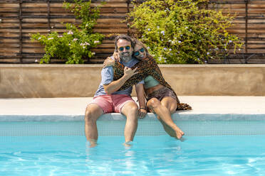 Glückliche reife Frau umarmt Mann sitzt am Pool an einem sonnigen Tag - DLTSF03090