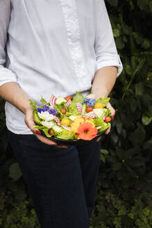 Midsection of woman holding bowl of vegan salad with vegetables and edible flowers - EVGF04078