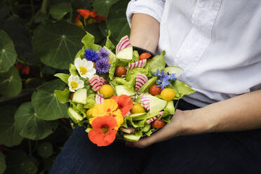 Mittelteil einer Frau, die eine Schüssel mit veganem Salat mit Gemüse und essbaren Blumen hält - EVGF04080