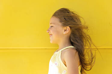 Happy girl with long hair standing in front of yellow wall - MEGF00013