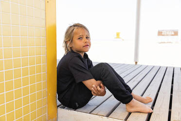 Sad blond boy sitting on wooden flooring - MEGF00038