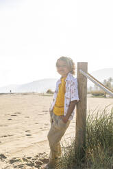 Smiling boy standing by pole on sunny day at beach - MEGF00054