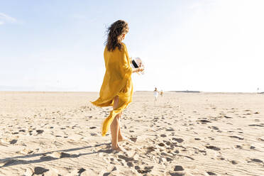 Frau mit Hut am Strand stehend an einem sonnigen Tag - MEGF00063