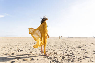 Ältere Frau mit Hut steht am Strand an einem sonnigen Tag - MEGF00064