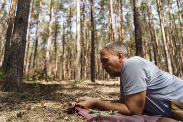 Älterer Mann mit Smartphone im Wald liegend - TOF00089