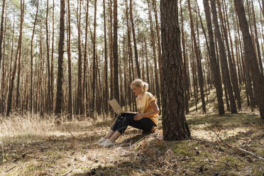 Mature woman using laptop in forest - TOF00090