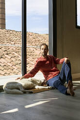 Thoughtful man with dog leaning on window - VEGF05878