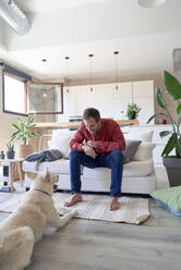 Man sitting on sofa in front of his dog at home - VEGF05885