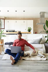 Smiling freelancer working on laptop sitting by dog at home - VEGF05891