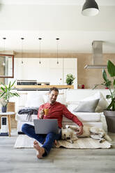 Glücklicher Geschäftsmann trinkt Kaffee mit seinem Hund im Wohnzimmer liegend - VEGF05898