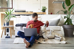 Businessman having coffee and feeding dog at home - VEGF05900