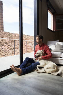 Nachdenklicher Mann sitzt mit Hund und schaut durch das Fenster - VEGF05912