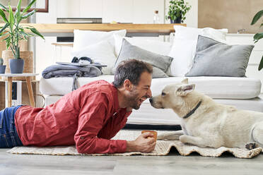 Glücklicher Mann mit Kaffeetasse, der mit seinem Hund zu Hause liegt - VEGF05916