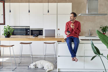 Contemplative man with mobile phone eating apple at home - VEGF05924