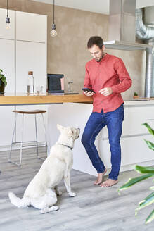 Man using mobile phone standing in front of dog - VEGF05926