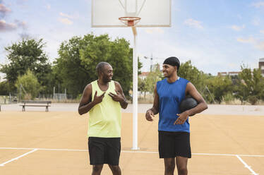 Lächelnder junger Mann mit Ball im Gespräch mit seinem Vater auf dem Basketballplatz - JCCMF07166