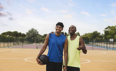 Lächelnder Vater im Gespräch mit seinem Sohn, der auf dem Basketballplatz gestikuliert - JCCMF07178