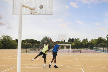 Young man throwing basketball in hoop playing with father at sports court - JCCMF07180