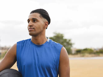 Contemplative young man with basketball at sports court - JCCMF07192